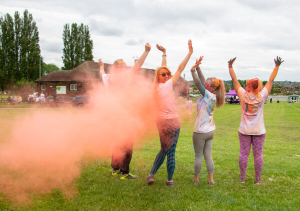 4 women with their arms up facing away from the camera. A cloud of paint powder about to cover them